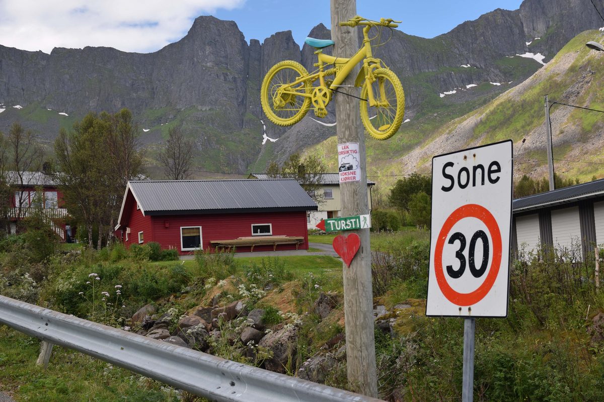 Fartsgrenseskilt «Sone 30» ved veien i Mefjordvær på Senja, med rødt hus og bratte fjell bak