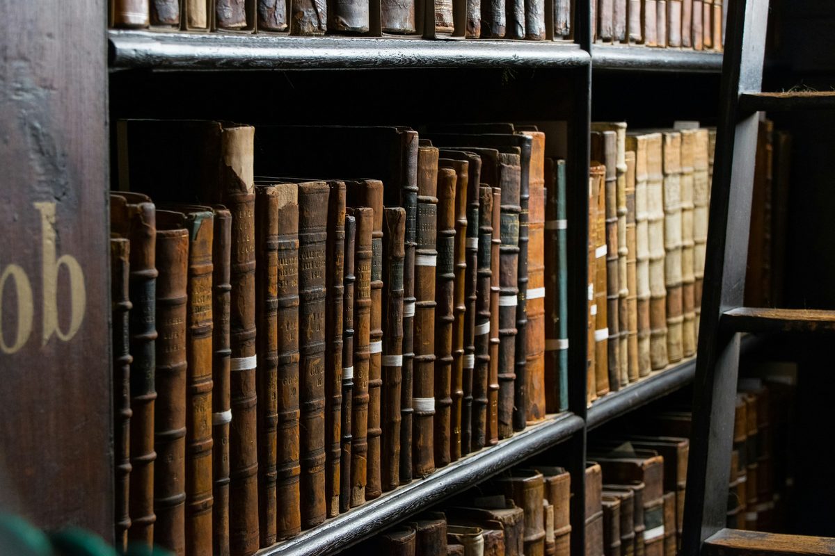 Gamle innbundne bøker på mørke trehyller i et bibliotek